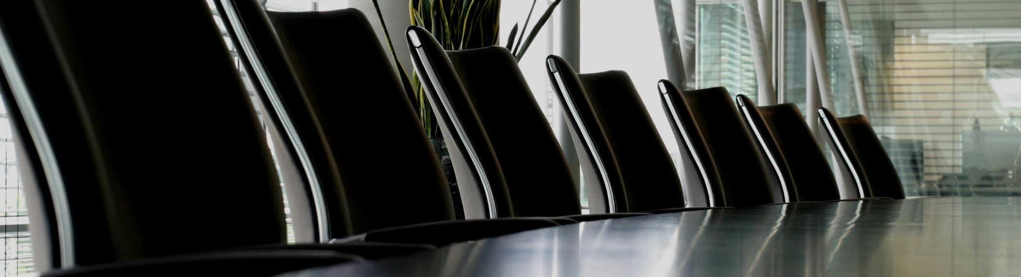 Black seats at a boardroom table in a room with windows